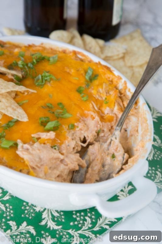A baking dish filled with hot and bubbly barbecue chicken dip, garnished with green onions and a spoon ready for serving.