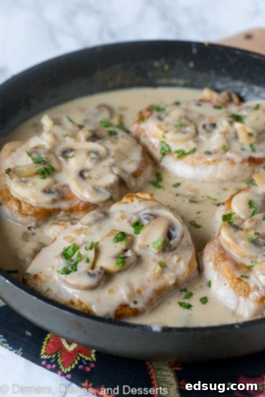Smothered pork chops with mushroom gravy in a skillet.