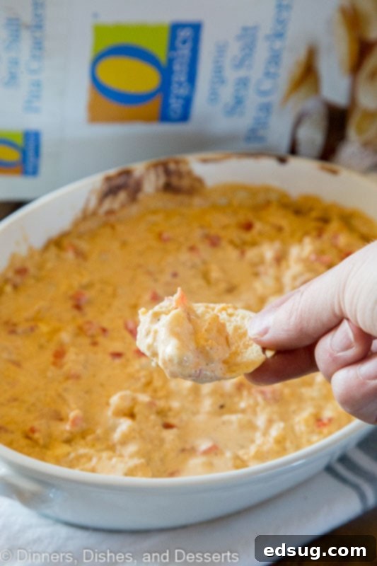 A serving of spicy shrimp dip on a table with a cracker scooping out a portion of the dip