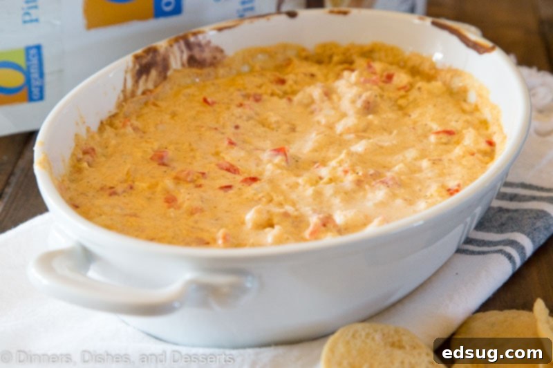 Close up shot of a creamy, cheesy shrimp dip in a white bowl, showing texture and ingredients