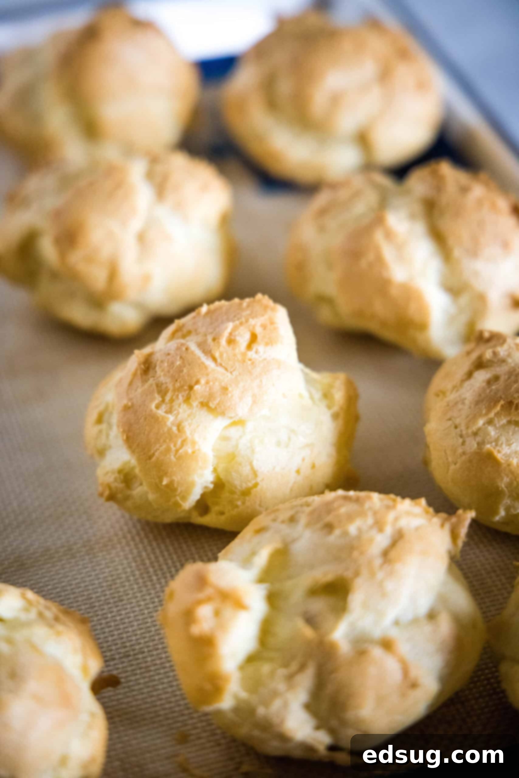 Baked cream puffs on a lined baking sheet.