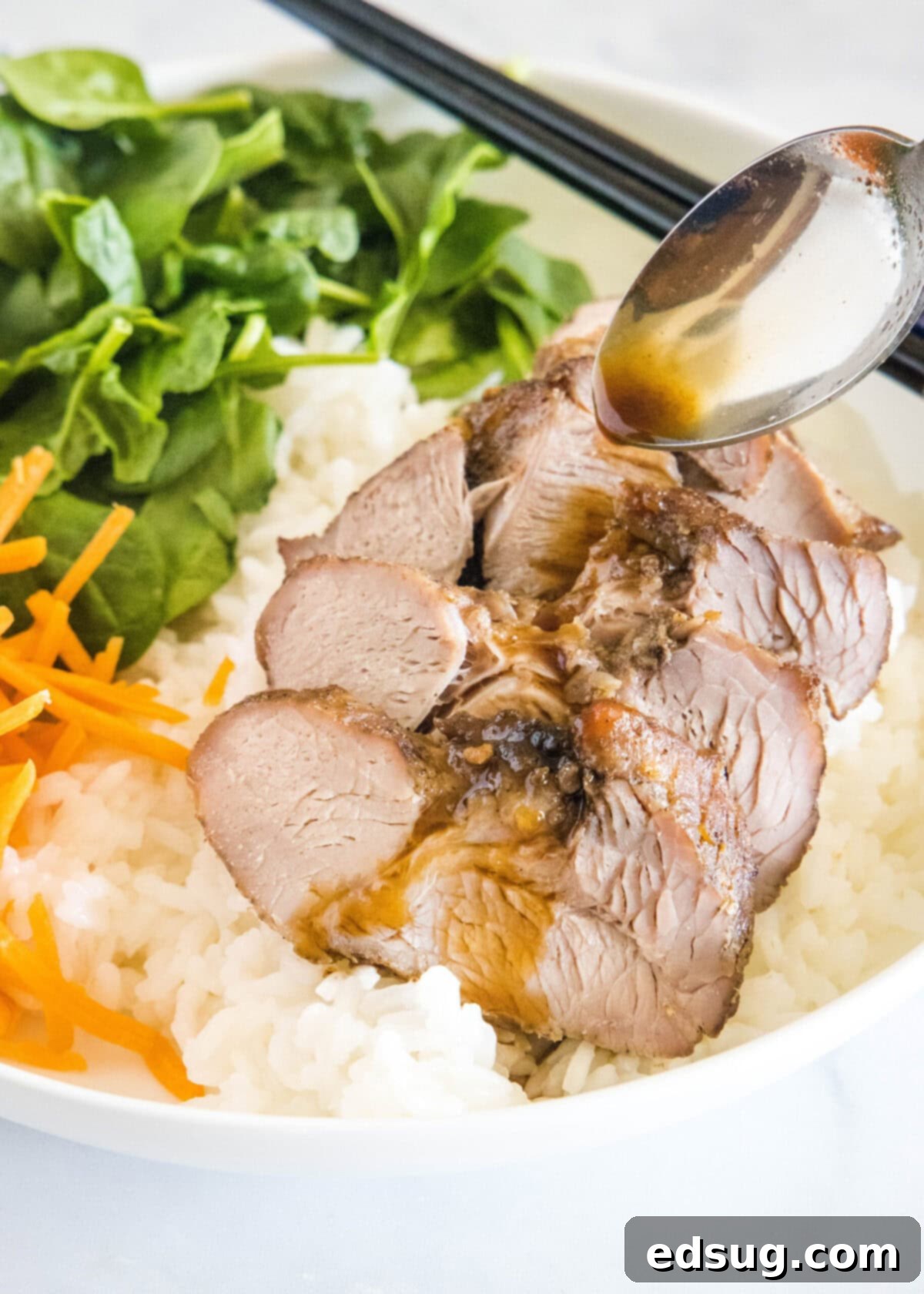 This easy char siu pork recipe is tender, juicy, and loaded with your favorite Chinese flavors like hoisin and five-spice powder. A spoon spooning sauce over char siu pork on a bed of rid, next to carrots and cucumbers