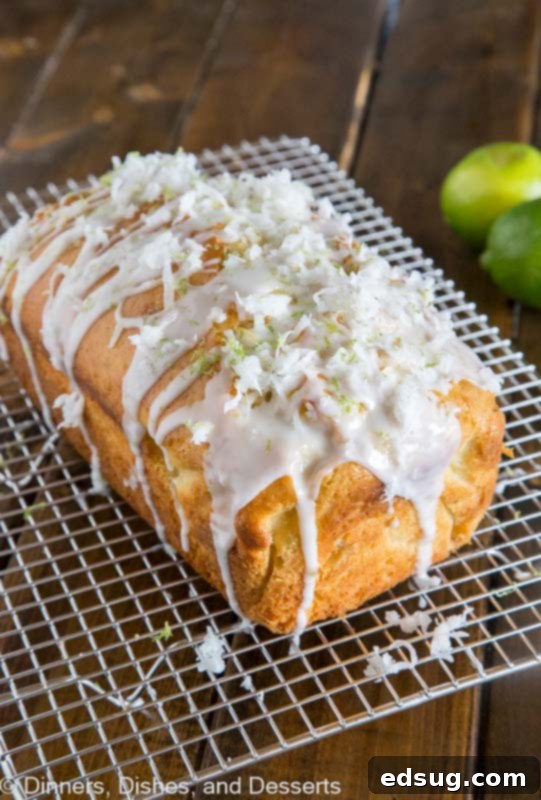 A golden-brown loaf of coconut lime quick bread on a cooling rack, drizzled with a white lime glaze and garnished with coconut flakes.