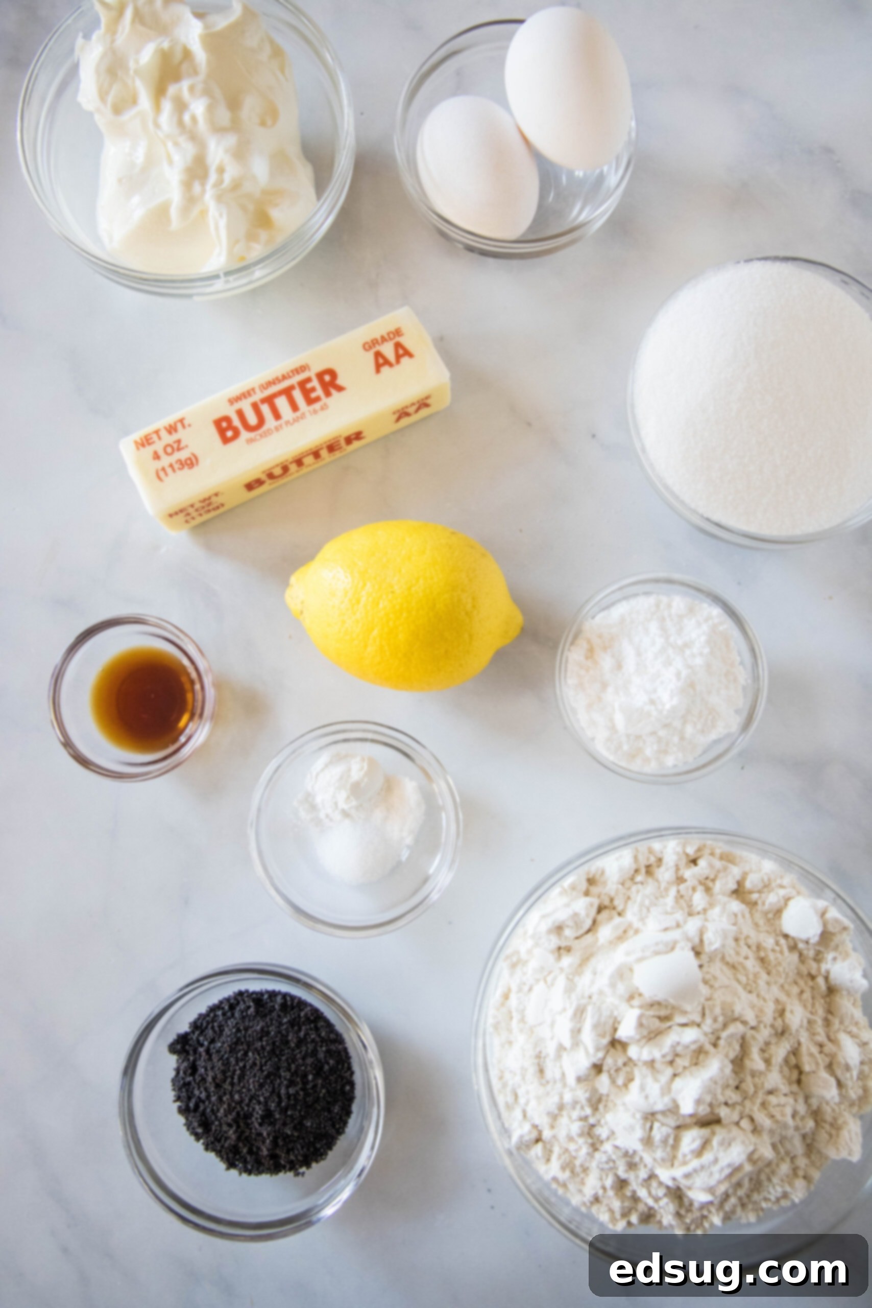 A vibrant flat lay image showcasing all the fresh ingredients for lemon poppy seed muffins, including lemons, eggs, flour, sugar, butter, and Greek yogurt.
