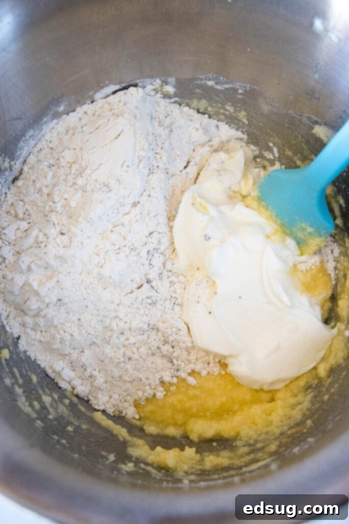Lemon poppy seed muffin batter ingredients combined in a mixing bowl with a blue rubber spatula, showing a thick, pale yellow batter.