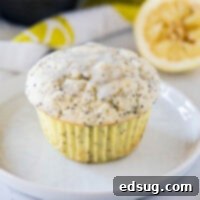 Close up of a lemon poppy seed muffin on a white plate, showcasing its texture and glaze.