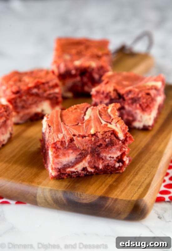 Decadent Red Velvet Cheesecake Brownies 3 Red velvet cheesecake swirl brownies arranged neatly on a wooden cutting board, ready to be served.