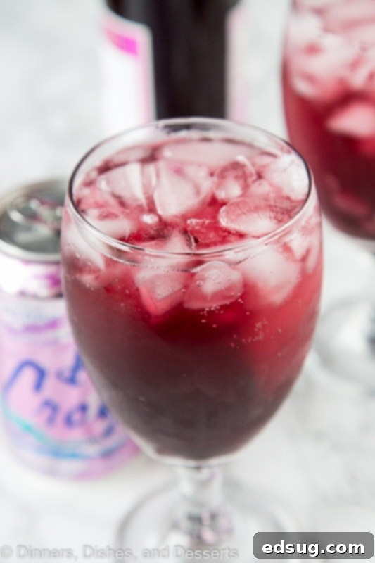 close up of a berry red wine spritzer in a glass, showing its vibrant color and garnish