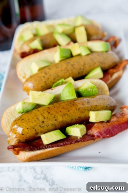 Grilled brats topped with diced avocado and crispy bacon on a plate, ready to serve.