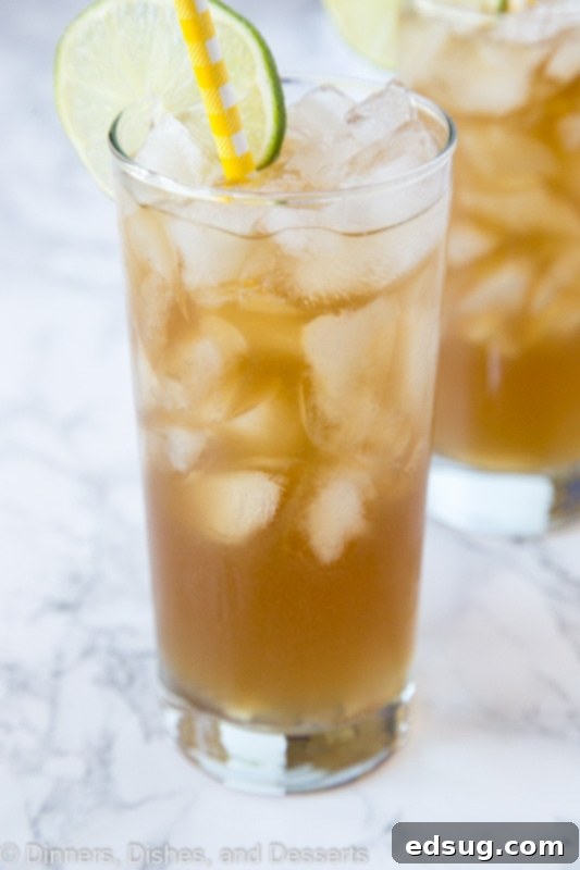 A glass of long island iced tea with ice and a straw, against a blurred background