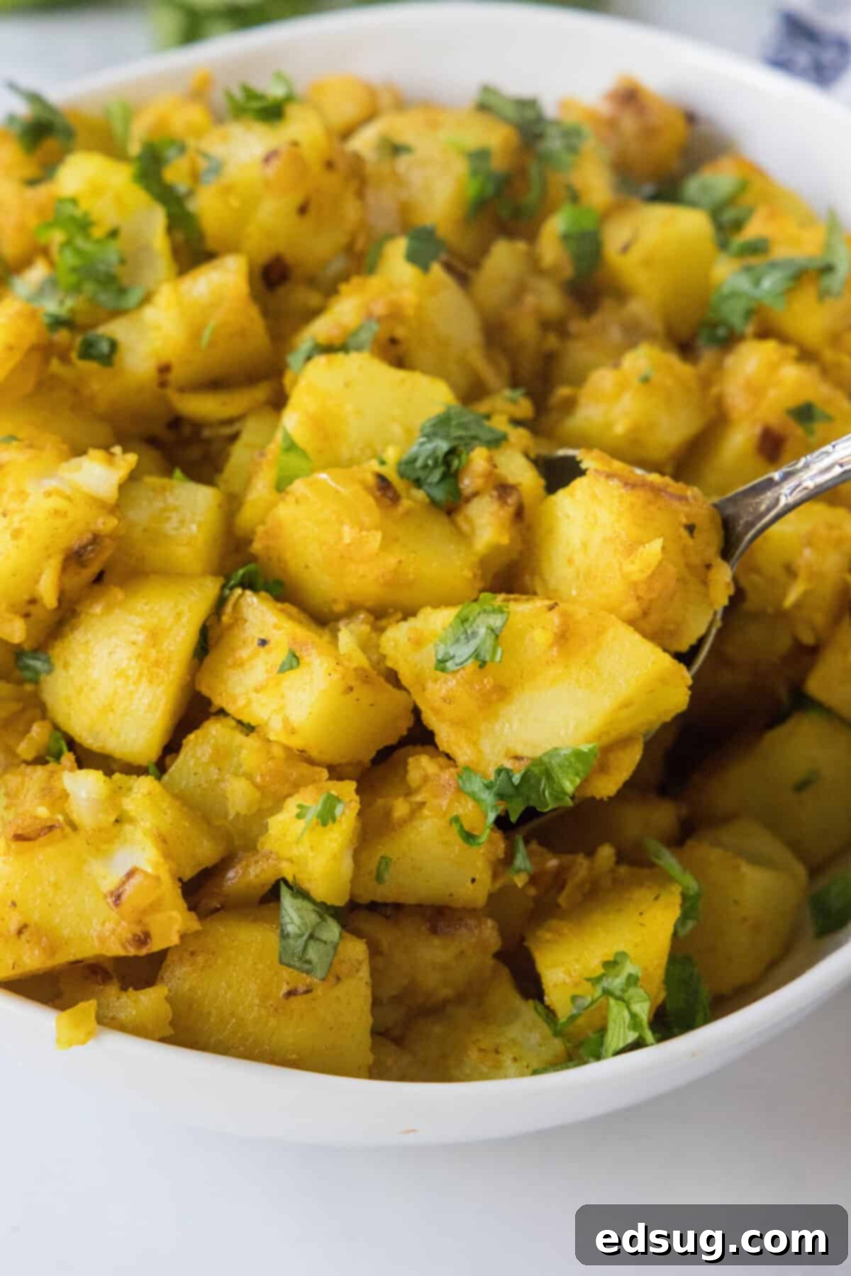 Scooping golden curried potatoes out of a rustic serving dish, ready to be enjoyed.