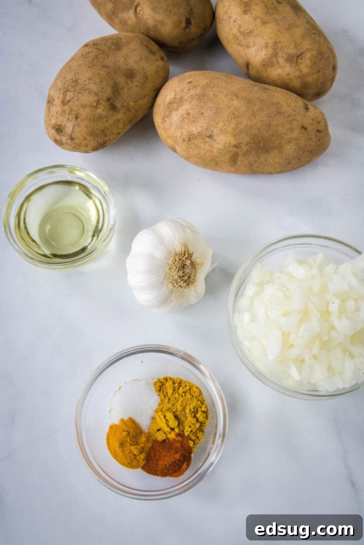 A beautiful flat lay of all the fresh ingredients needed for curried potatoes, including diced potatoes, onions, garlic, and an array of colorful spices.