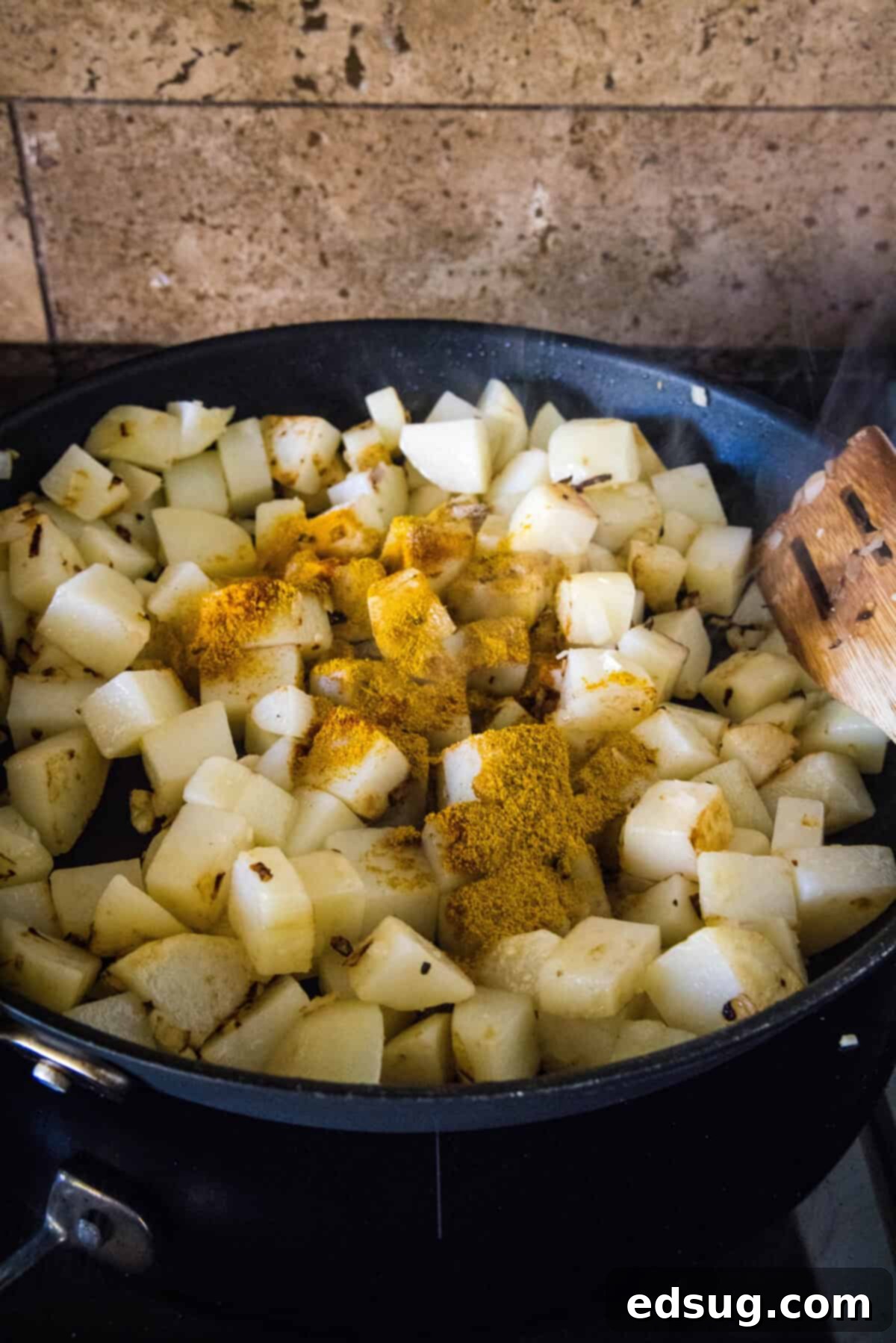 Diced potatoes simmering in a skillet, coated with a generous sprinkle of vibrant curry powder and other spices.