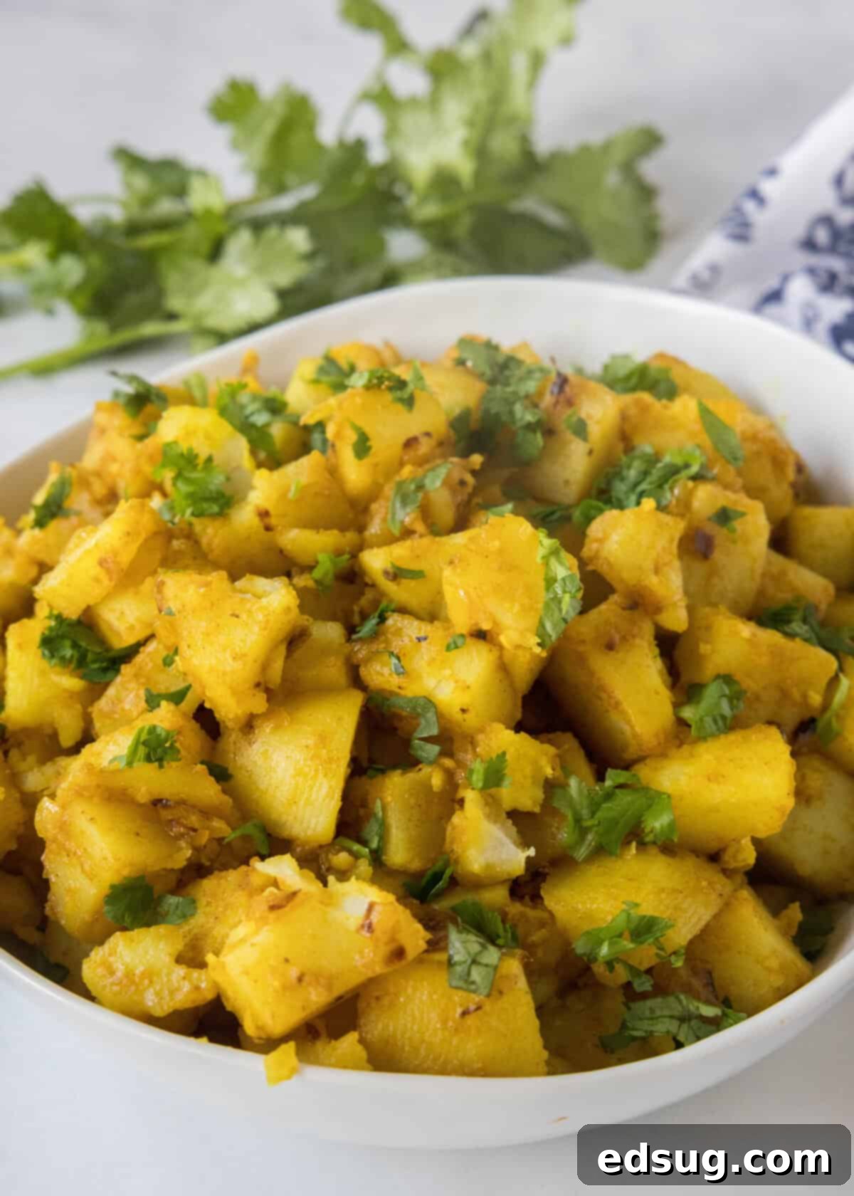 A beautiful serving bowl filled with golden curried potatoes, generously topped with fresh green cilantro, ready to be enjoyed.