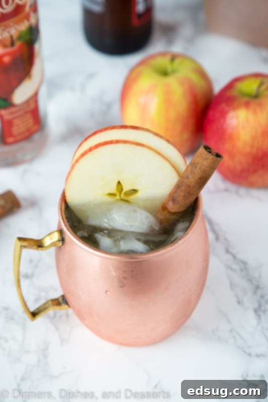 A close-up of an Apple Cider Moscow Mule in a copper mug, garnished with apple slices