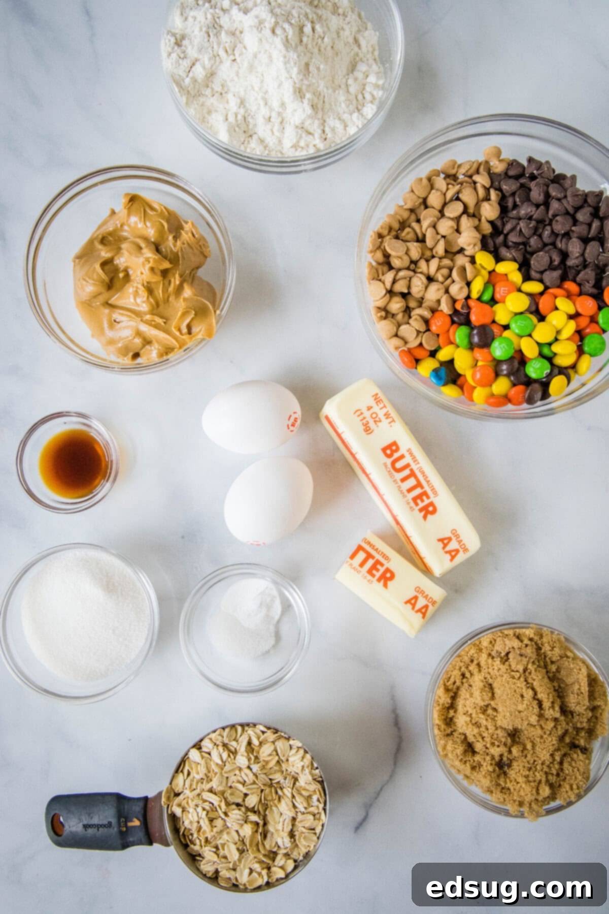 Assortment of monster cookie ingredients laid out, including oats, flour, M&M's, chocolate chips, and peanut butter chips.