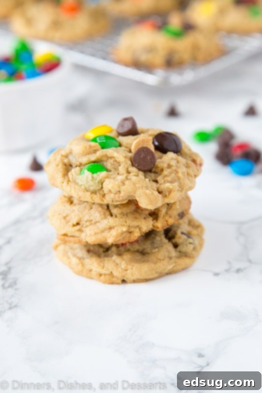 Stack of golden brown monster cookies with visible M&M's and chocolate chips on a kitchen countertop.