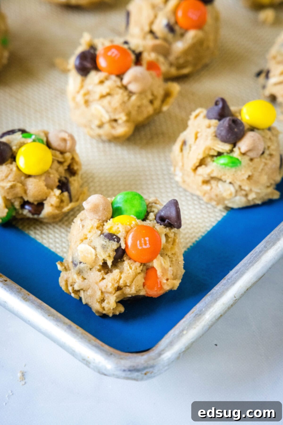 Unbaked monster cookie dough balls, topped with extra M&M's, arranged on a baking sheet ready for the oven.