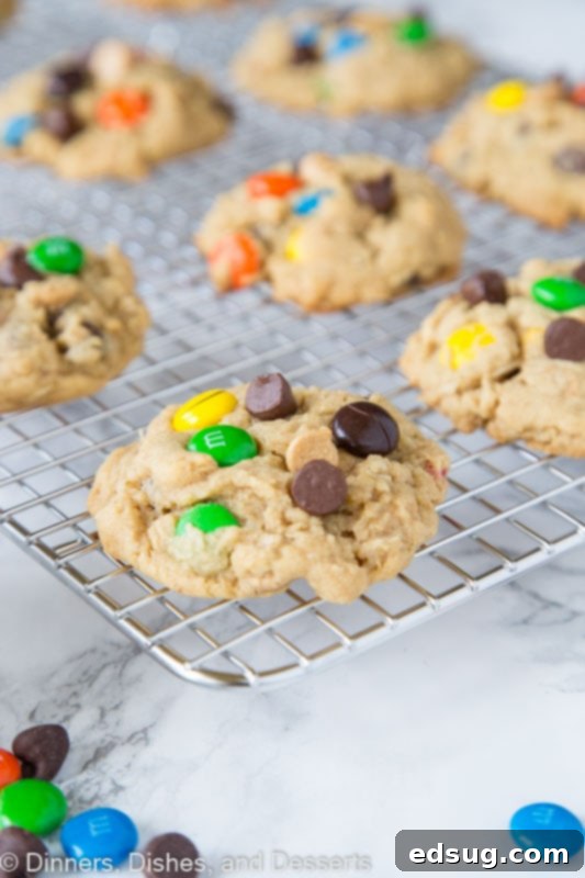 Close-up of a warm, freshly baked monster cookie with melted chocolate and vibrant M&M's on a cooling rack.