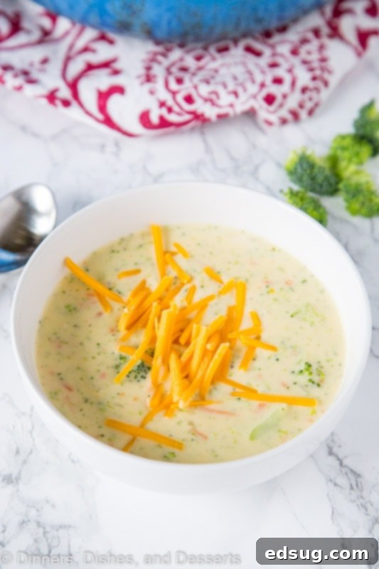 A close-up of a bowl of broccoli cheese soup, garnished with shredded cheddar cheese, ready to be served.