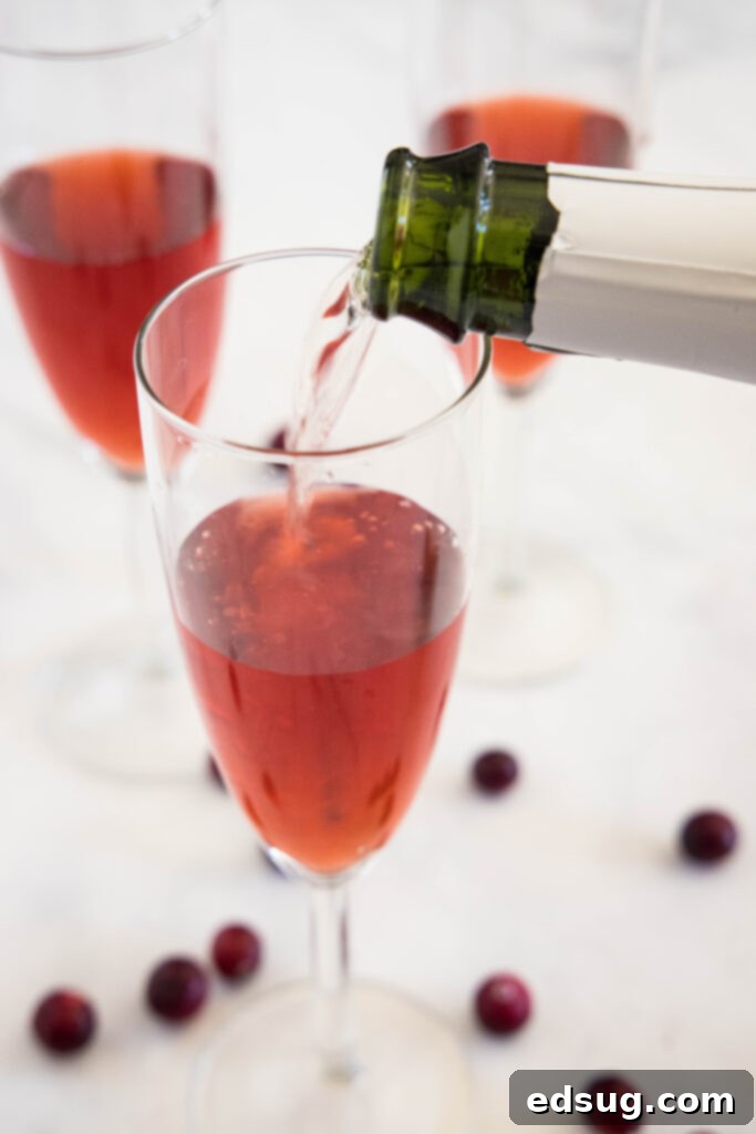 Pouring sparkling wine into a glass with cranberry juice for a Cranberry Mimosa