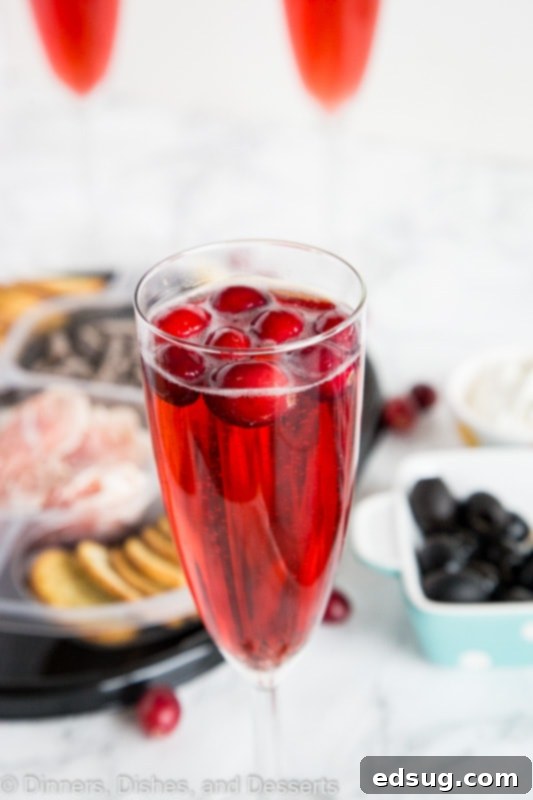 A close-up of a Cranberry Mimosa in a wine glass, with festive dinner elements blurred in the background