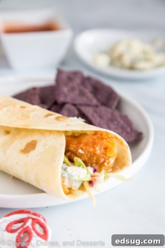A fresh Crispy Buffalo Chicken Wrap, perfectly rolled and ready to eat, served on a casual paper plate.