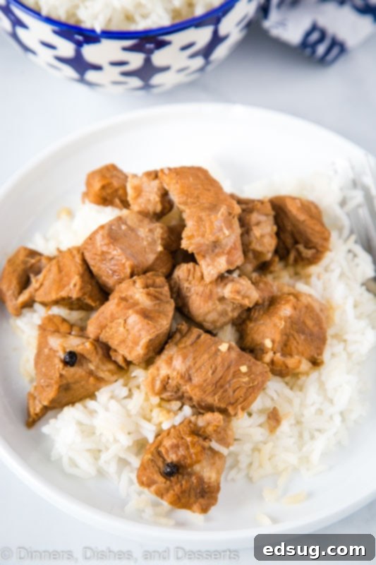 Filipino style adobo made with pork shoulder or pork butt, simmering in a pot with a rich, dark sauce.