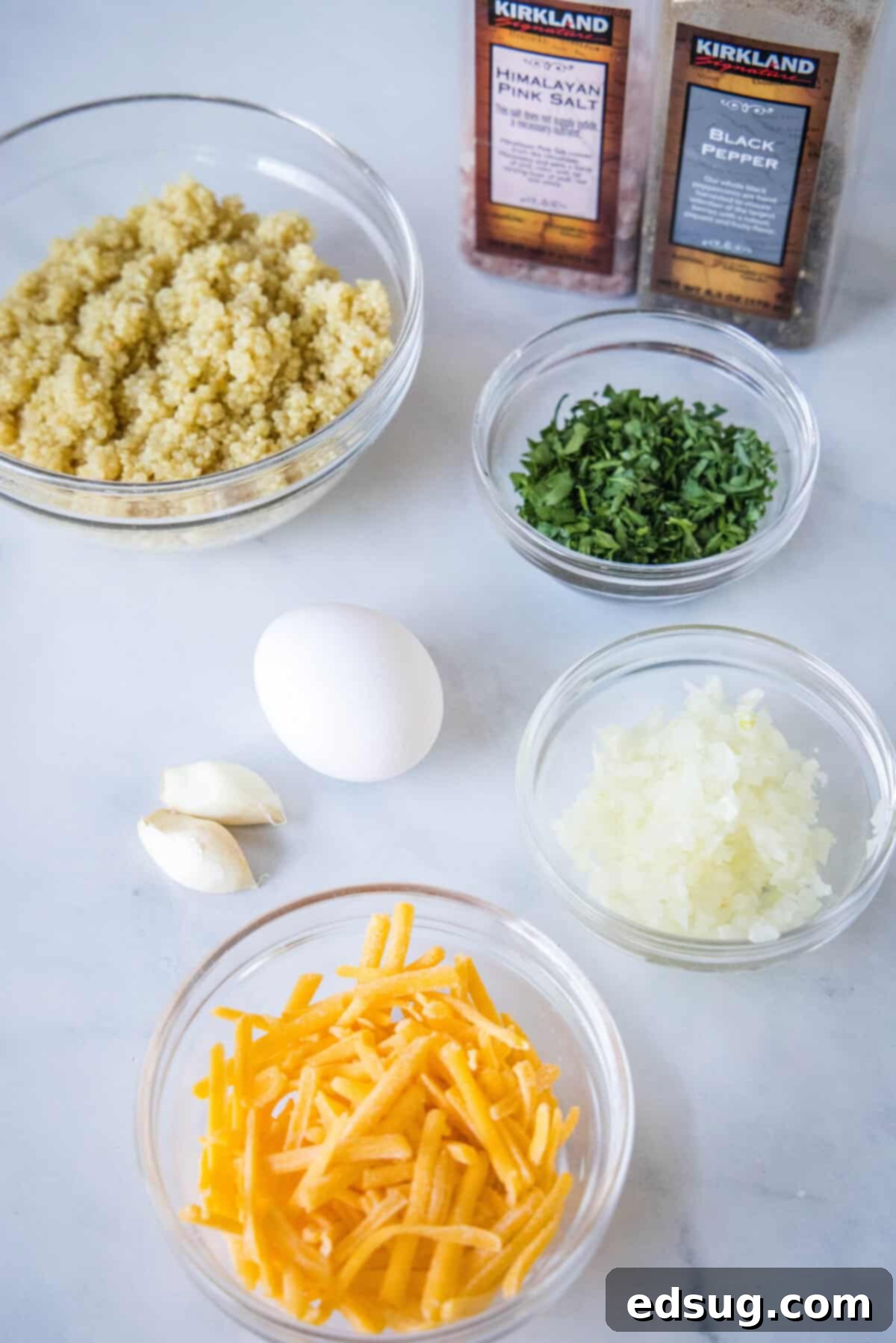 A selection of fresh ingredients laid out, including cooked quinoa, shredded cheddar cheese, eggs, finely chopped onions, fresh parsley, and garlic cloves, ready for mixing.