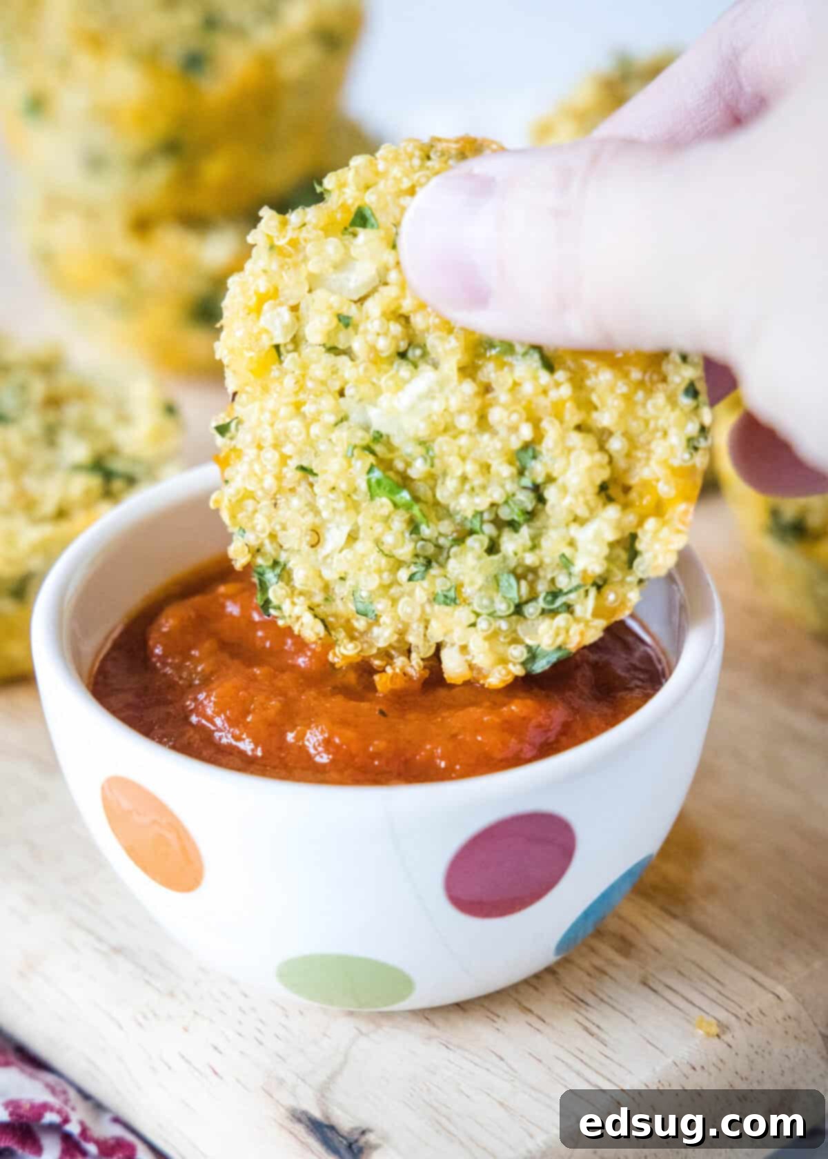 A close-up of a single golden quinoa bite being dipped into a small bowl of marinara sauce, showcasing its perfect texture and readiness for enjoyment.