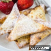 Close up of a pile of crispy dessert wontons covered in powdered sugar next to fresh strawberries and a fork, highlighting their irresistible texture.