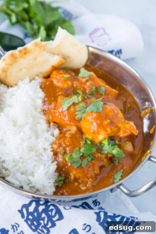 Close-up of Chicken Vindaloo curry in a bowl, garnished with fresh cilantro, with naan bread and rice in the background, showcasing a complete and flavorful Indian meal.