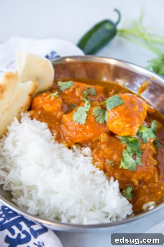A serving of Chicken Vindaloo with chicken chunks and rich, red sauce, next to a portion of white rice in a bowl, garnished with fresh herbs, showcasing a perfect spicy meal.
