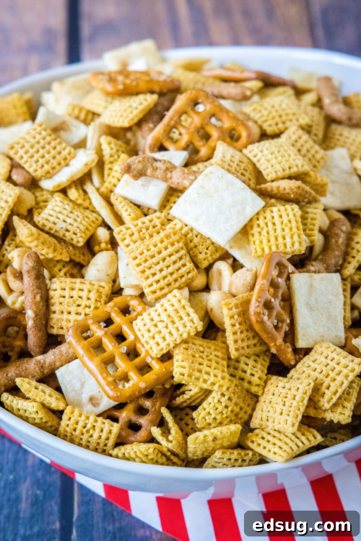 Mexican Snack Mix_labeled A vibrant serving bowl overflowing with homemade Mexican snack mix, featuring golden cereals, assorted nuts, and crispy pretzels, all glistening with savory spices.