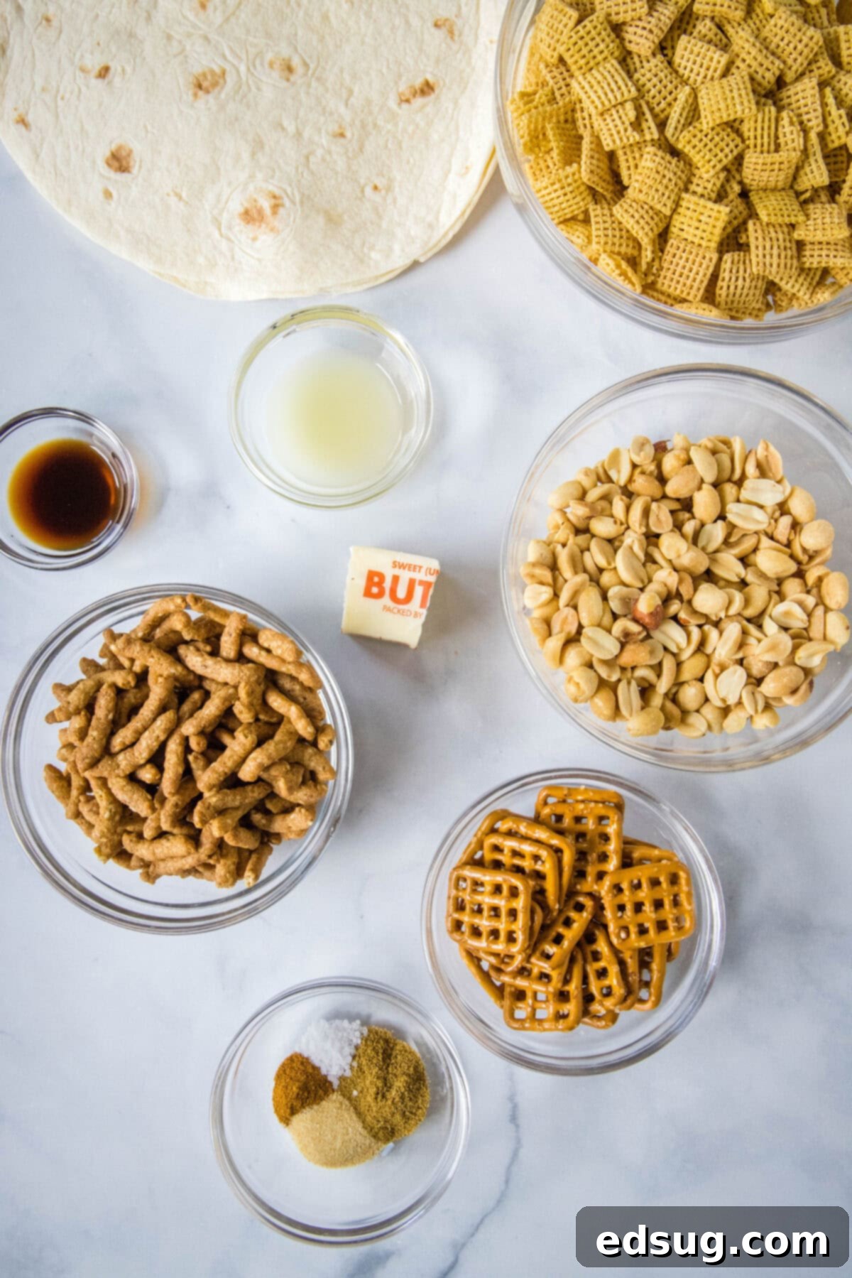 Fiesta Taco Crunch 3 Individual ingredients for the taco snack mix neatly arranged on a white surface, including corn chex, roasted peanuts, small pretzels, tortilla squares, sesame sticks, and various spices.