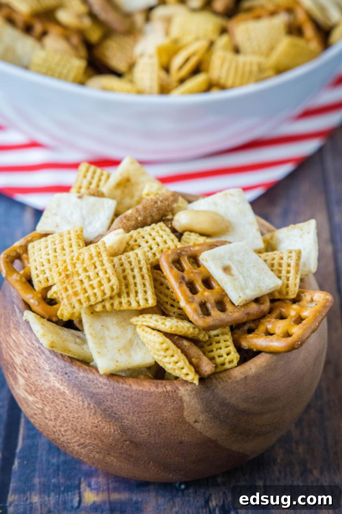 Mexican Snack Mix 2_ A large wooden serving bowl filled with a generous portion of Taco Snack Mix, with a smaller white bowl in the background, hinting at a party setting.