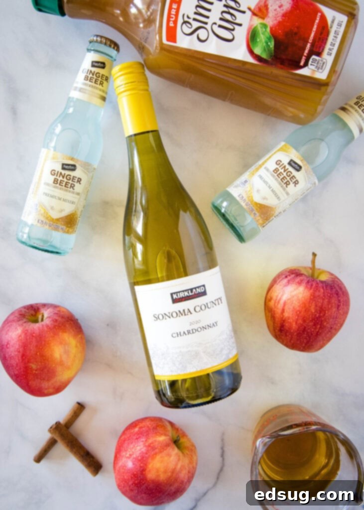 ingredients for fall sangria laid out on a table including apples, wine, rum, ginger beer, and cider