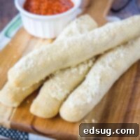 Four golden-brown copycat Crazy Breadsticks on a cutting board, with a ramekin of marinara sauce.