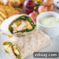 Two halves of a Chick-fil-A Cool Wrap on a plate, accompanied by dipping sauce, grapes, and potato chips.