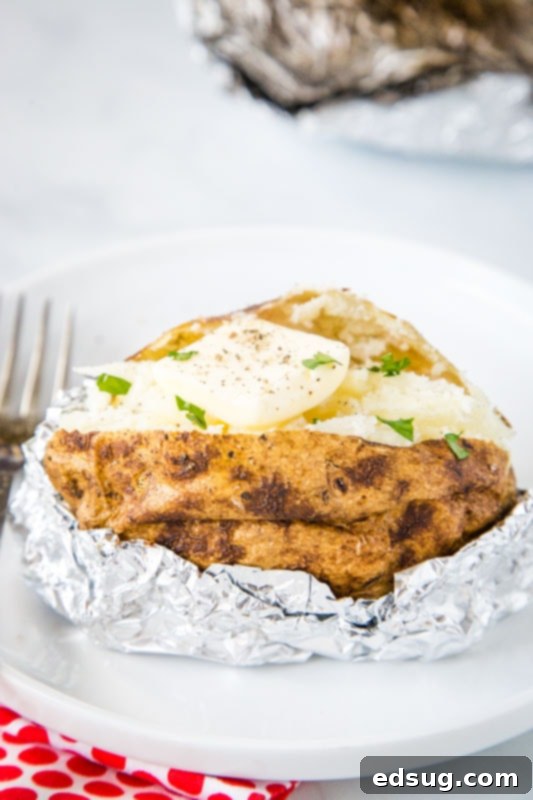 Grill-Baked Potatoes 3 baked potato in foil on white plate cut open with butter