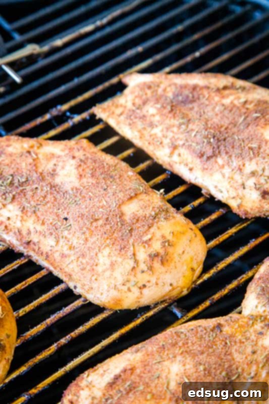 Smoked chicken breast cooking on a pellet smoker grill with visible smoke and heat.
