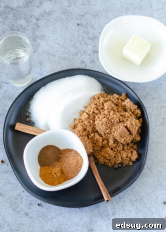 Various ingredients for hot buttered rum laid out: brown sugar, white sugar, cinnamon, nutmeg, allspice, butter, and a bottle of rum