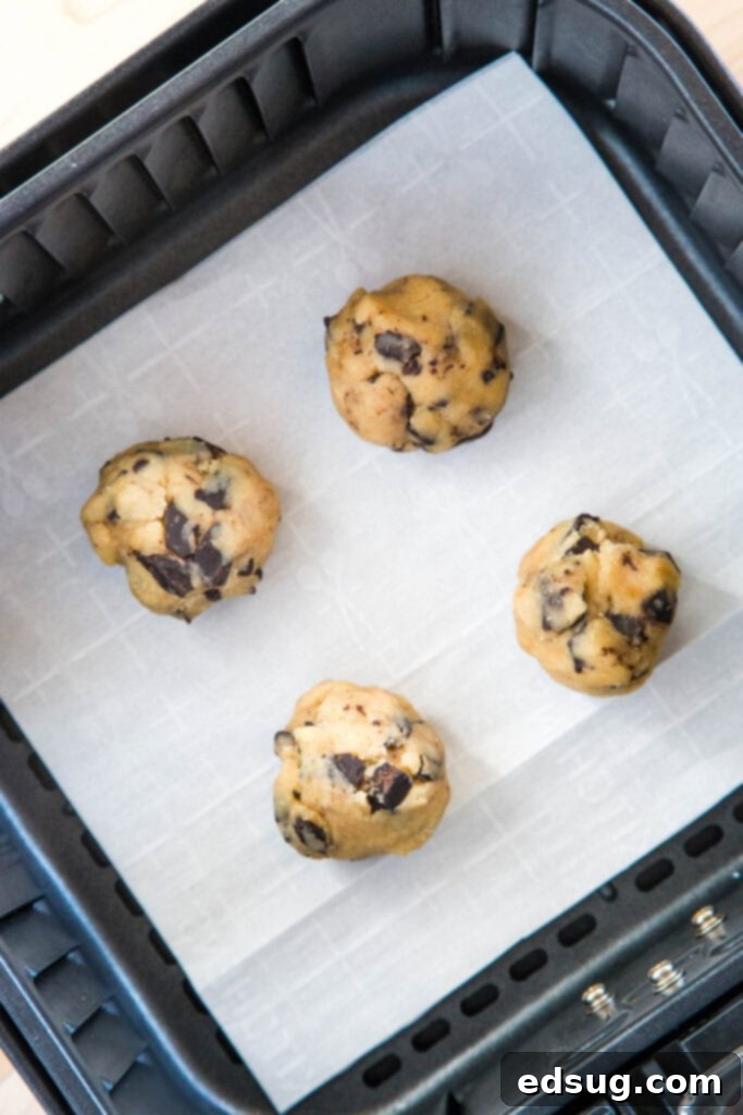 Raw balls of cookie dough arranged on parchment paper inside an air fryer basket, ready for baking.