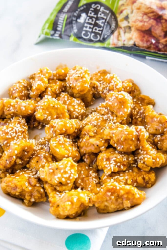 A close-up shot of sesame chicken pieces on a white plate, garnished with fresh sesame seeds.