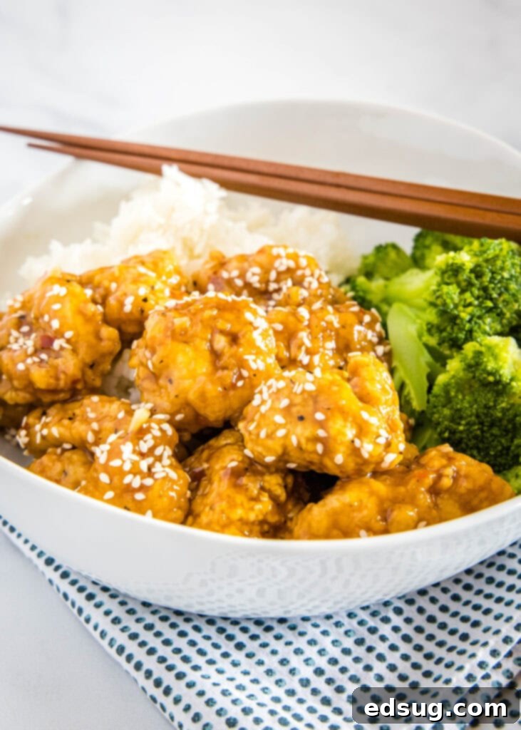 A bowl of delicious sesame chicken served with fresh green broccoli.