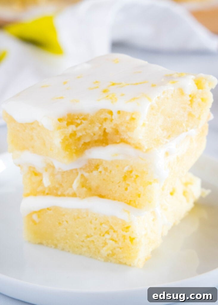 lemon brownies stacked on a plate with a bite taken out of the top one