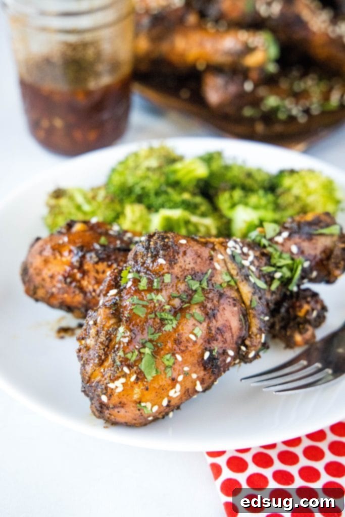 Grilled chicken leg on a plate, glistening with Asian BBQ sauce and garnished with fresh herbs