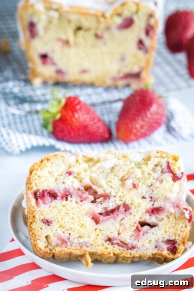 A perfectly sliced piece of super moist strawberry bread on a white plate, showcasing its tender crumb and abundant strawberry chunks.