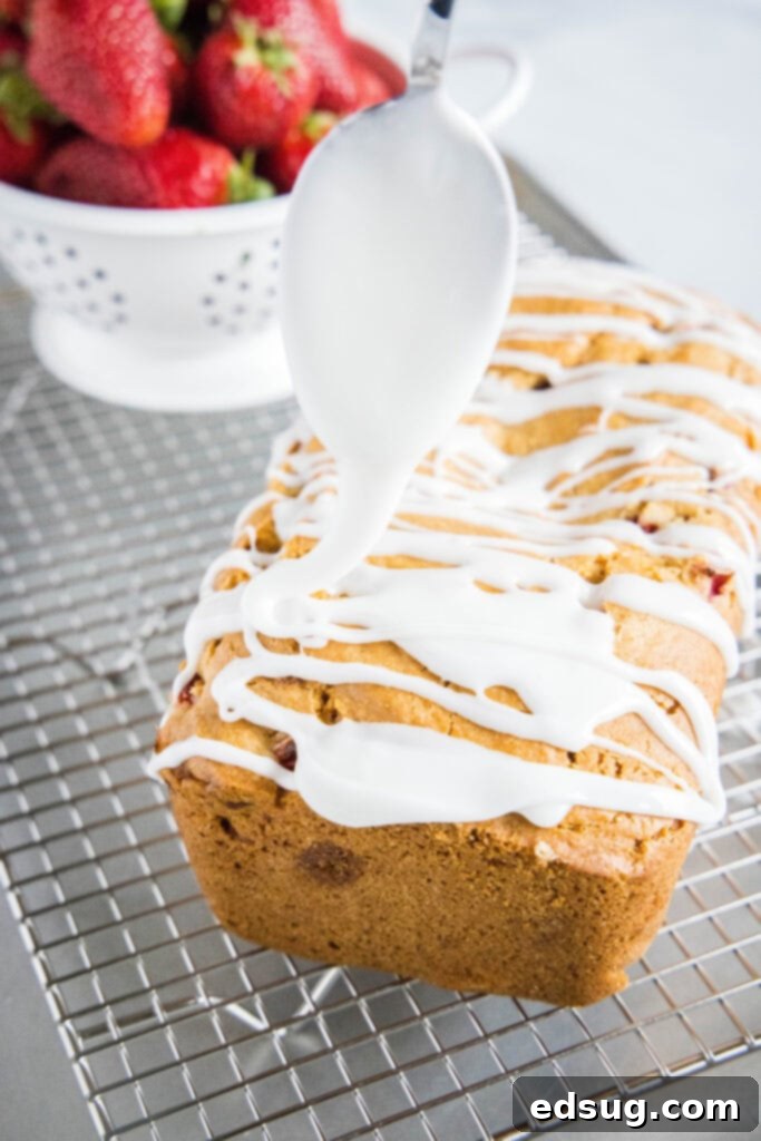 A delicious strawberry bread loaf being drizzled with a sweet white glaze on a cooling rack, the glaze slowly dripping down the sides.