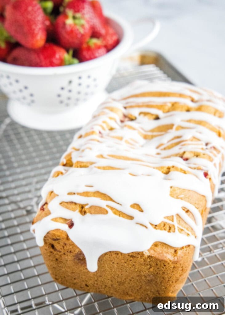 A beautifully glazed loaf of strawberry bread resting on a wire cooling rack, ready to be sliced and served.
